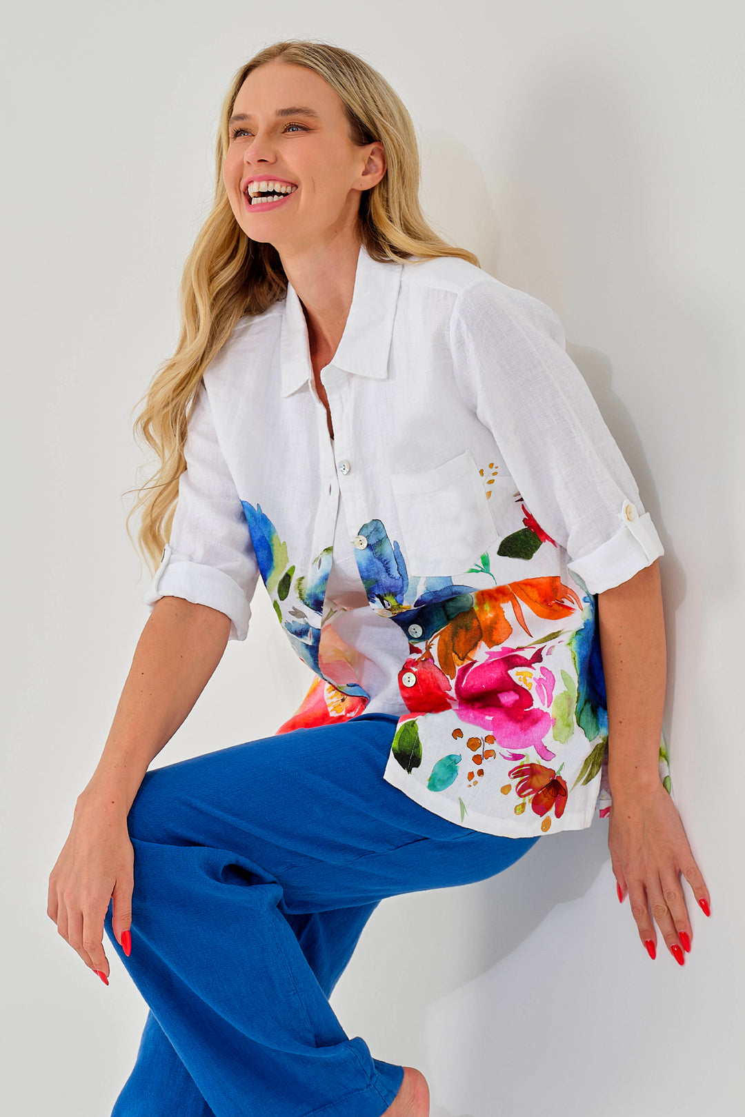 Woman wearing a loose white shirt with colorful floral design and blue pants against a white background