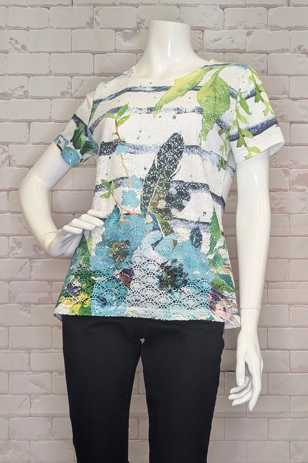 Mannequin wearing a colorful floral-patterned t-shirt against a brick wall.