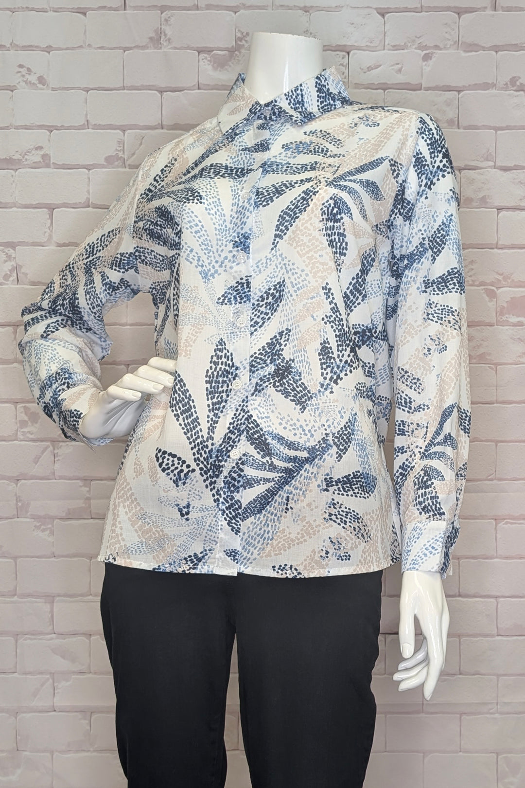 Mannequin wearing a long-sleeve shirt blouse with blue leaf pattern against a brick wall.