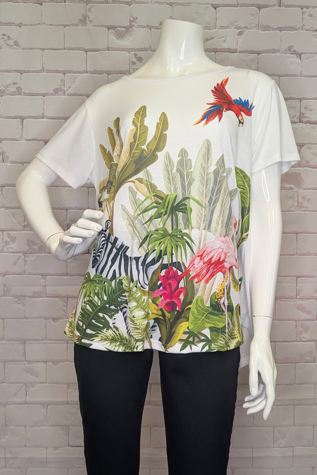 Mannequin wearing a white t-shirt with colorful tropical plant design against a brick wall.