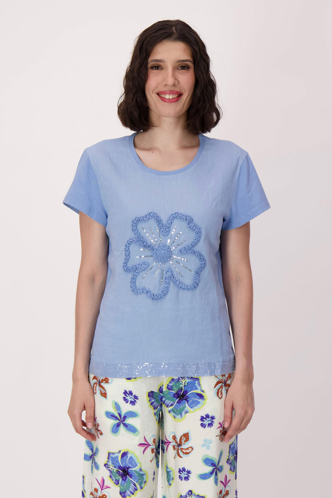 Woman wearing a blue t-shirt with a floral design and colorful pants on a light pink background