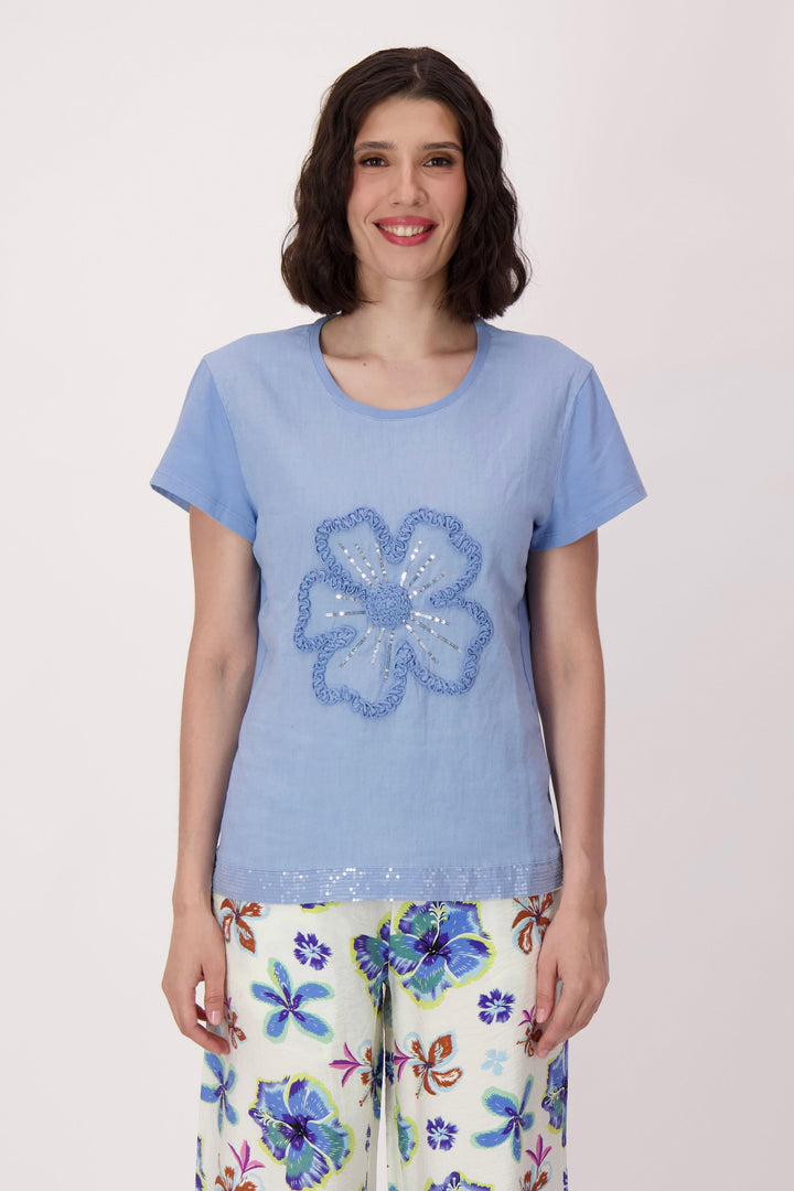 Woman wearing a blue t-shirt with a floral design and colorful pants on a light pink background