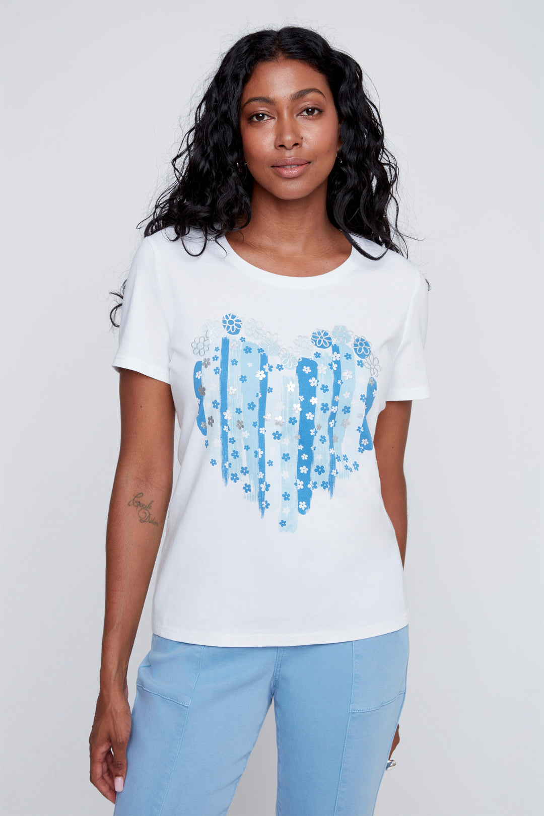 Woman wearing a white t-shirt with blue graphic heart design on a plain background
