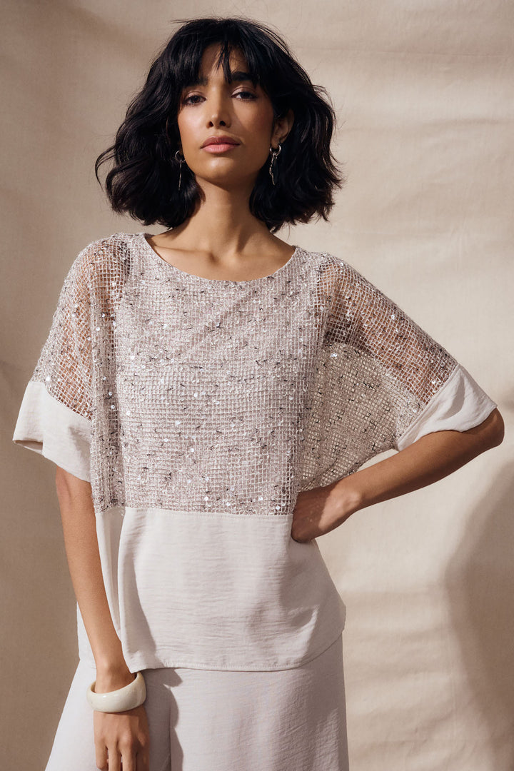 Woman wearing a sheer sequin top against a beige background