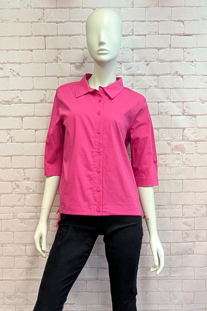 Mannequin wearing a pink shirt and black pants against a light brick wall.