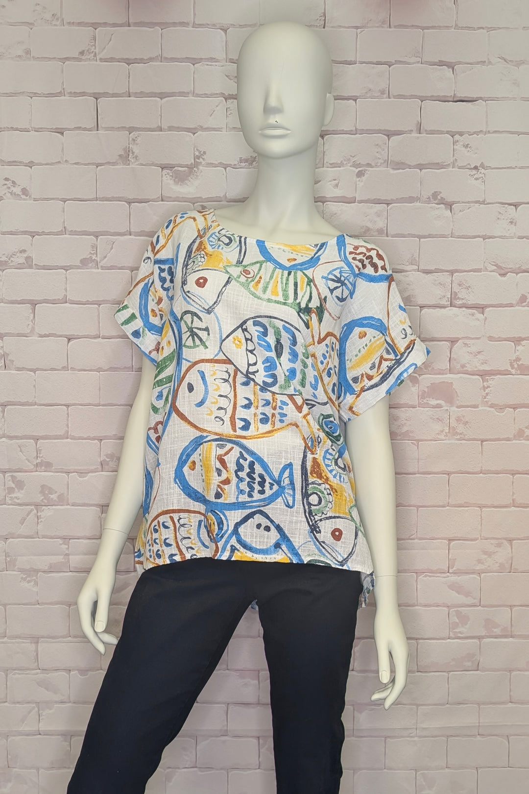 Mannequin wearing a colorful fish-patterned top against a brick wall.
