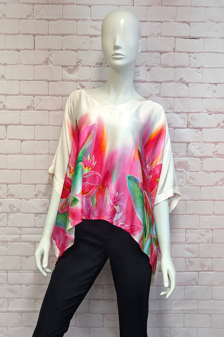 Mannequin wearing a colorful floral top with black pants against a light brick wall.