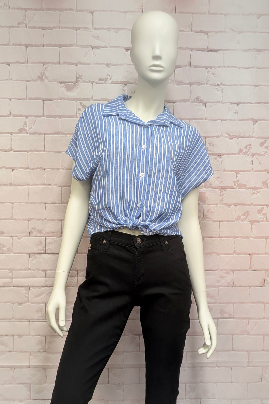 Mannequin wearing a blue and white striped shirt and black pants against a brick wall.