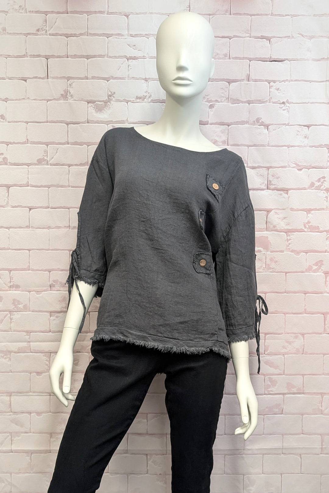 Mannequin wearing a gray top with tie sleeves and black pants against a brick wall.