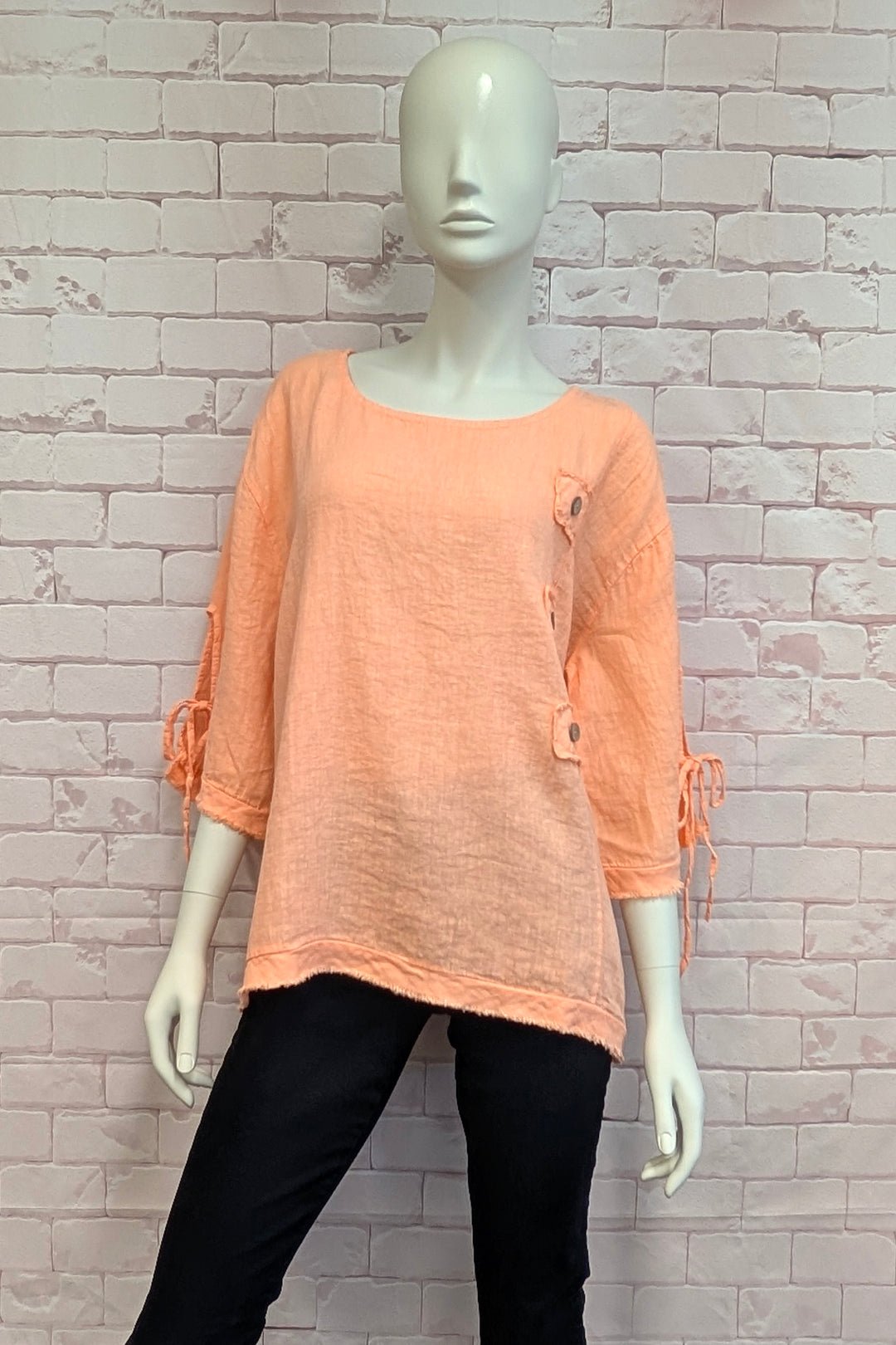 Mannequin wearing a peach-colored top with black pants against a light brick wall.