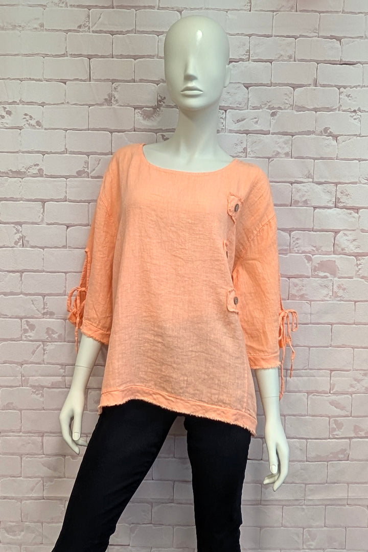 Mannequin wearing a peach-colored top with black pants against a light brick wall.