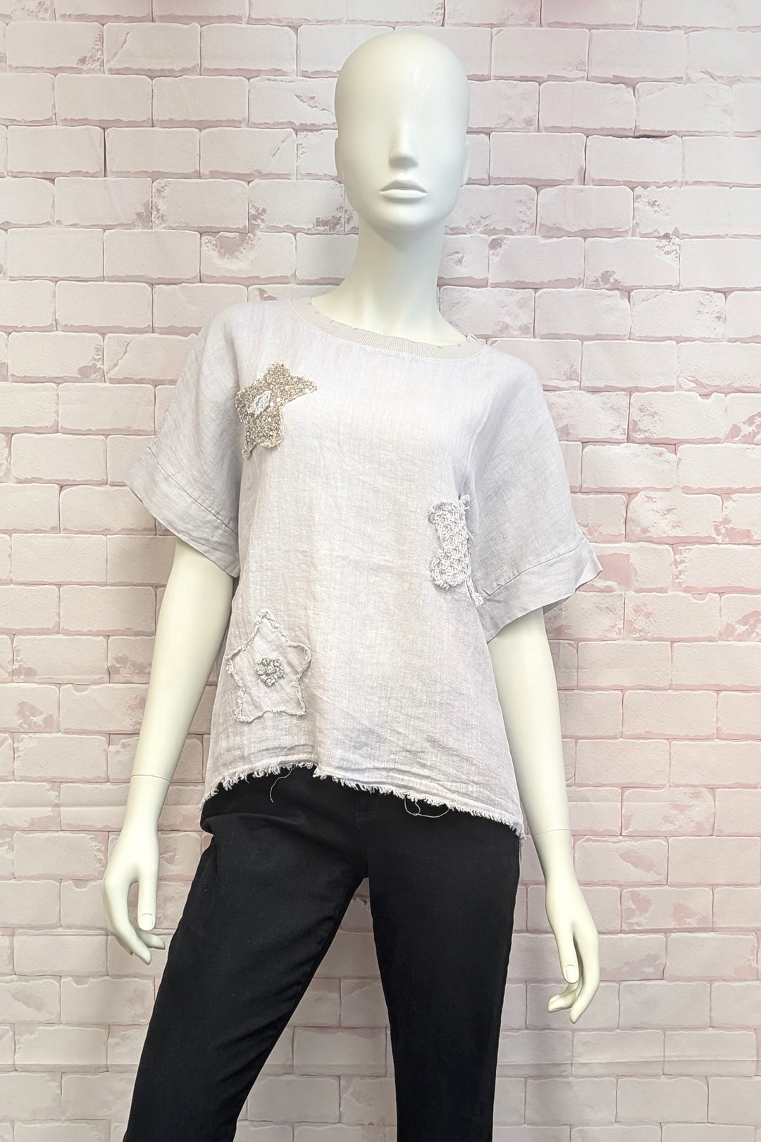 Mannequin wearing a light gray t-shirt with decorative elements against a white brick wall.