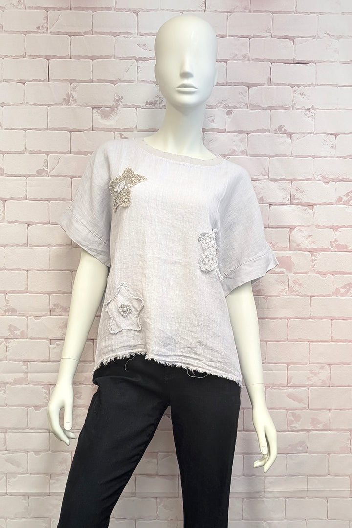 Mannequin wearing a light gray t-shirt with decorative elements against a white brick wall.