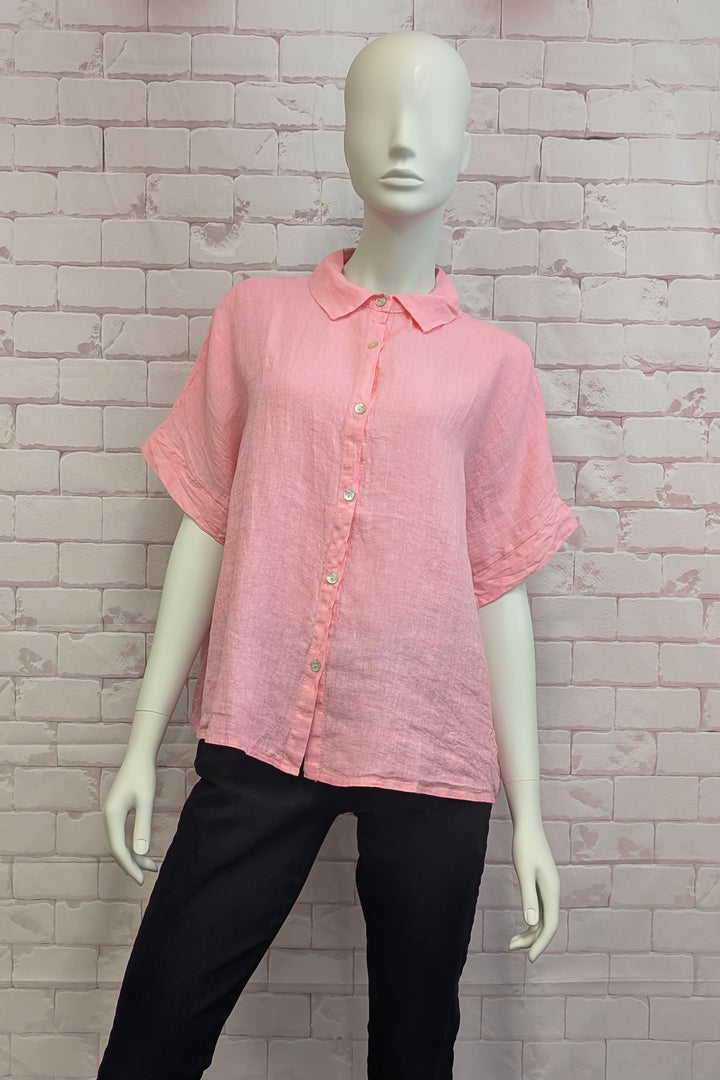 Mannequin wearing a pink short-sleeve button linen shirt against a brick wall.