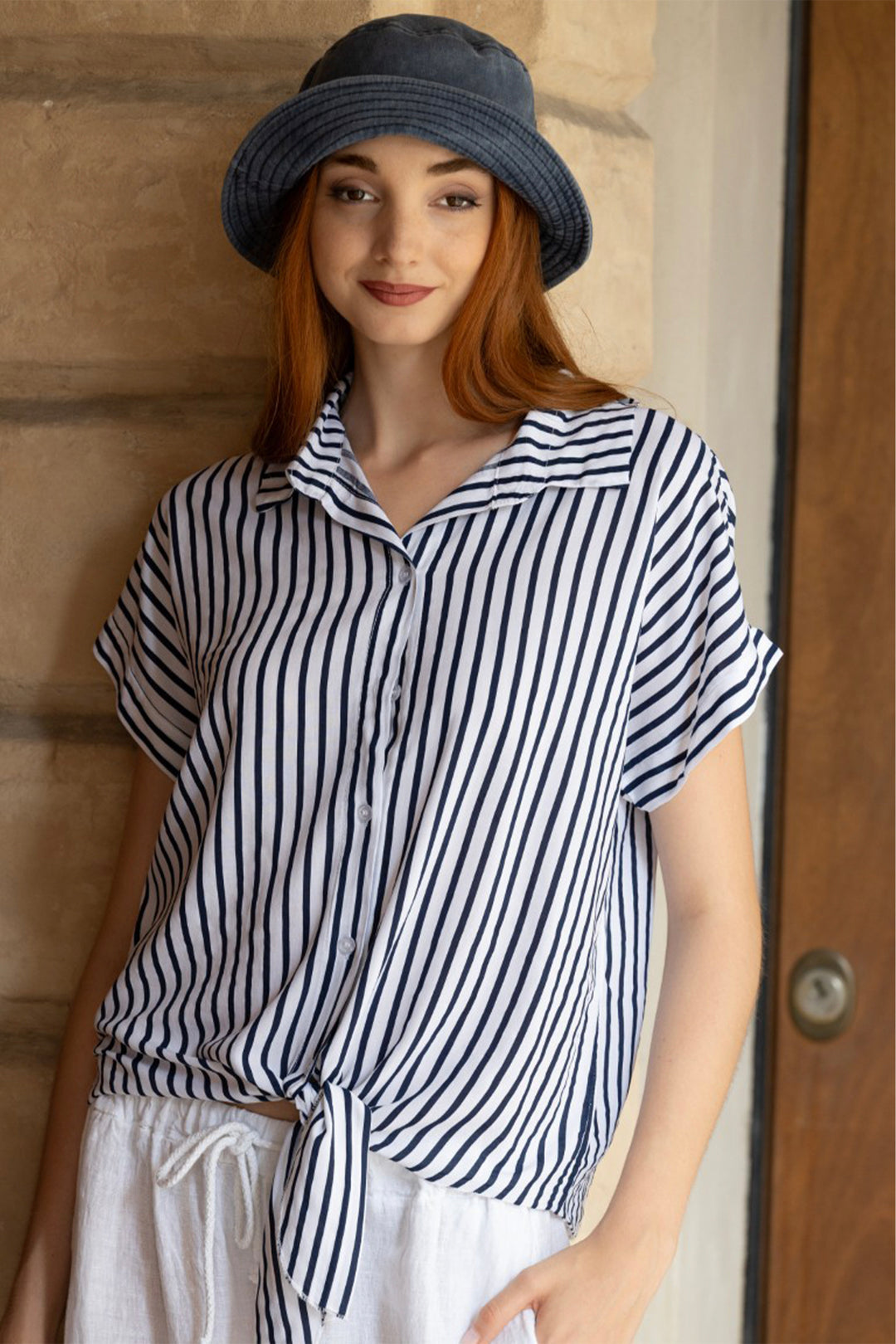 Woman wearing a striped button blouse and hat against a wooden door background