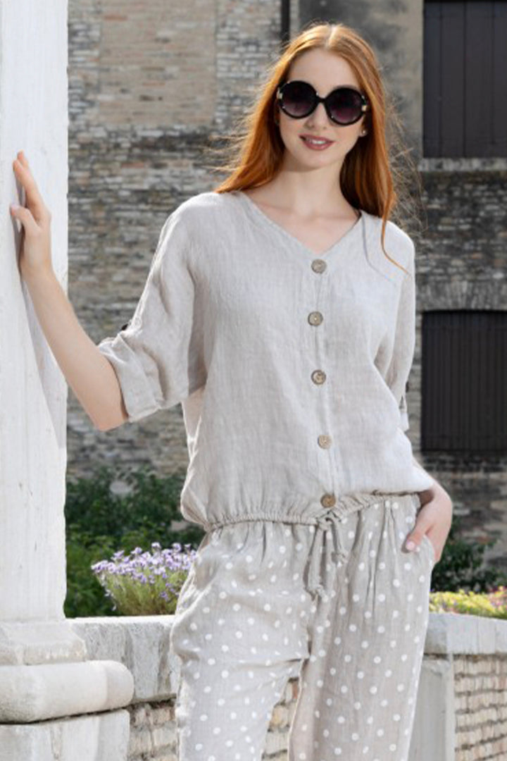 Woman wearing a light-colored button-up top and polka dot pants standing outdoors.