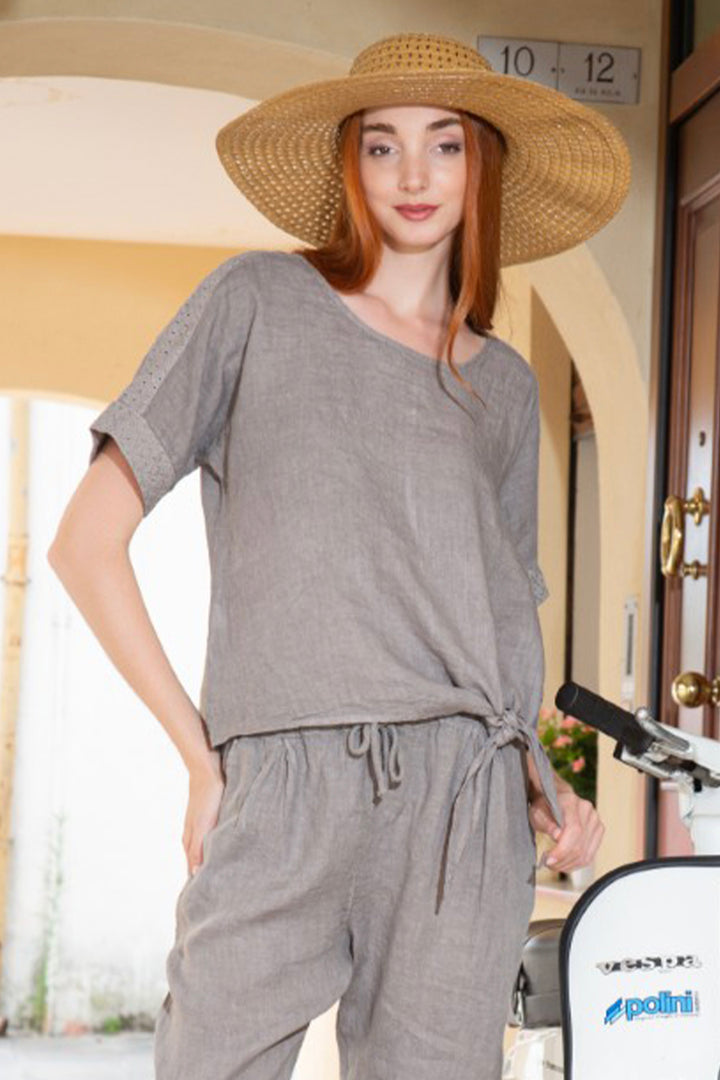 Woman wearing a gray linen top  standing next to a bicycle.