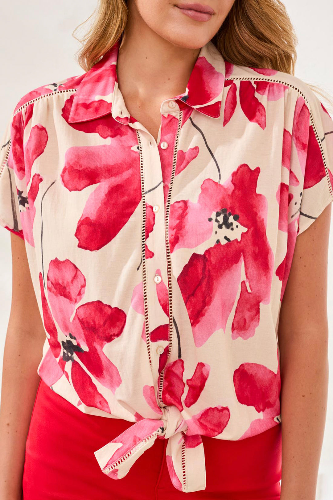 Woman wearing a floral button blouse with tie front, pink flowers on a white background