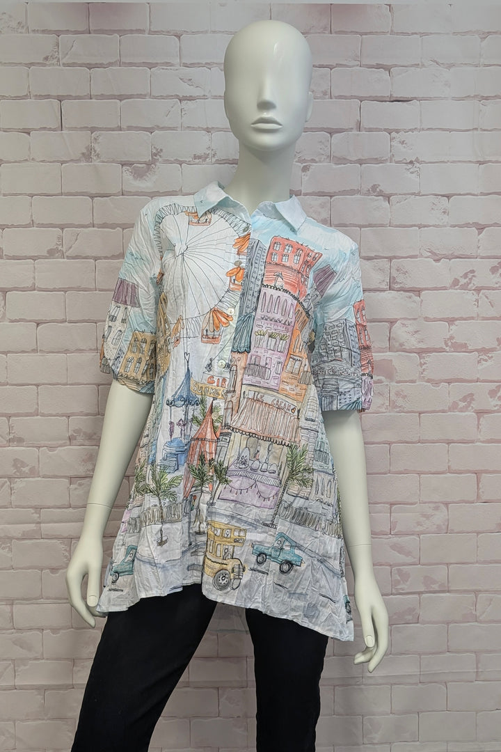 Mannequin wearing a patterned hi-lo button blouse against a brick wall background
