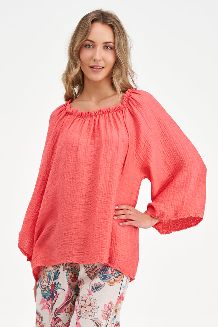 Woman wearing a coral blouse with floral pants on a white background