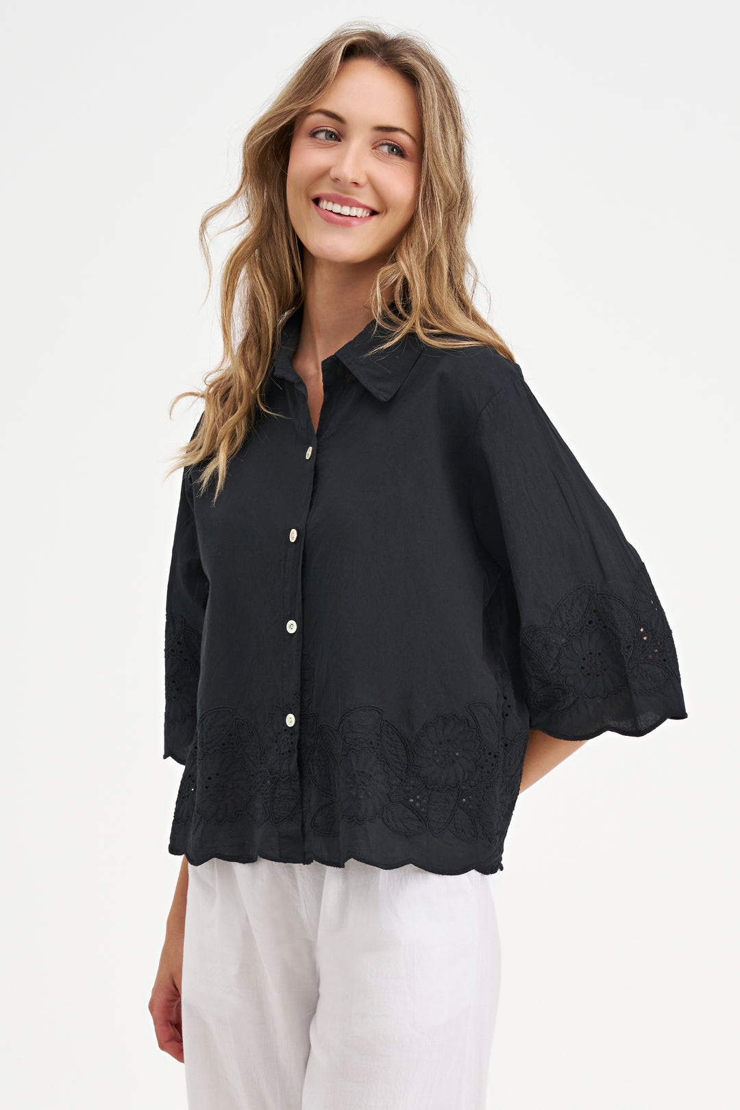 Woman wearing a black blouse with lace eyelet floral details on a white background