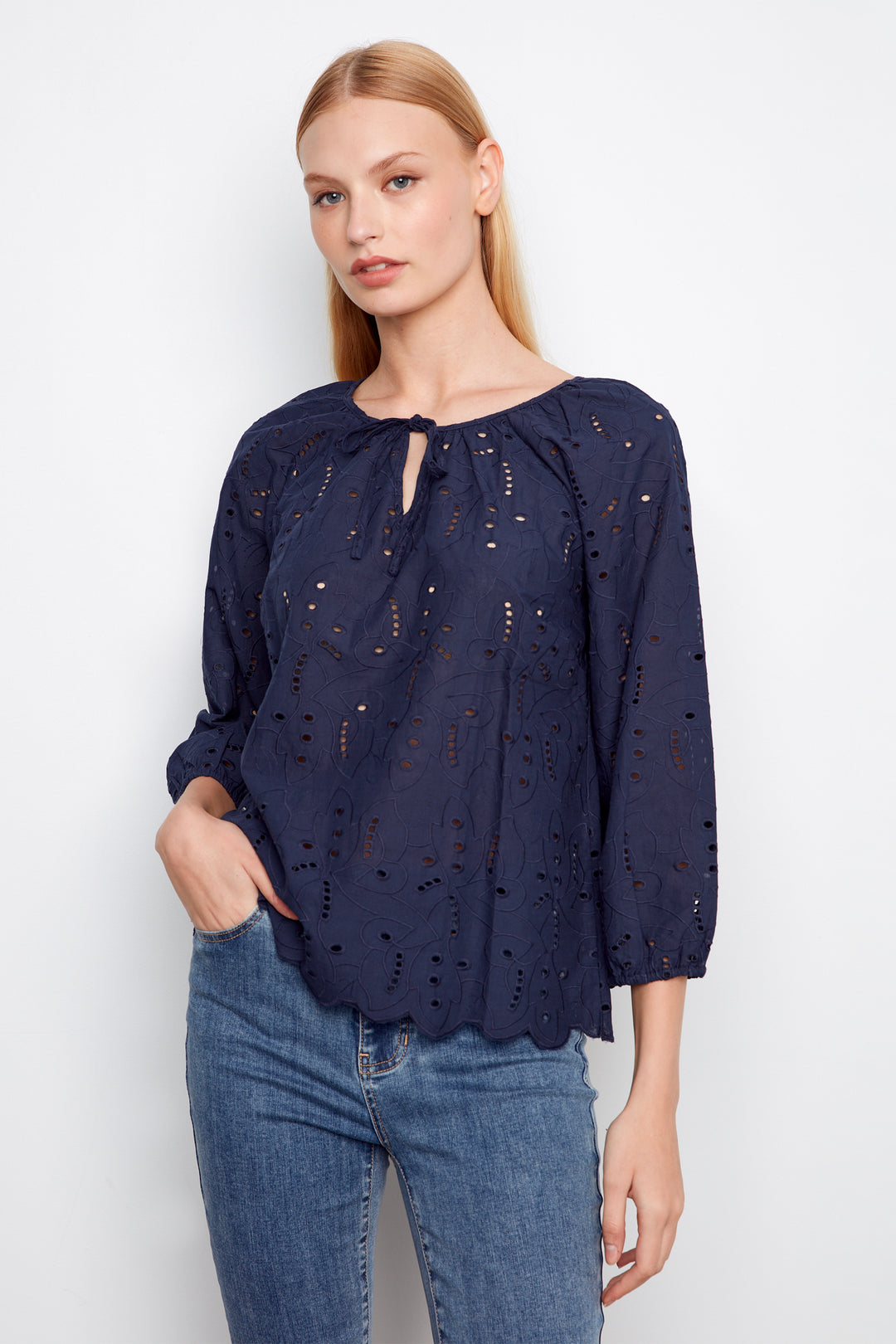 Woman wearing a navy blue blouse with intricate detailing cutouts and blue jeans on a white background