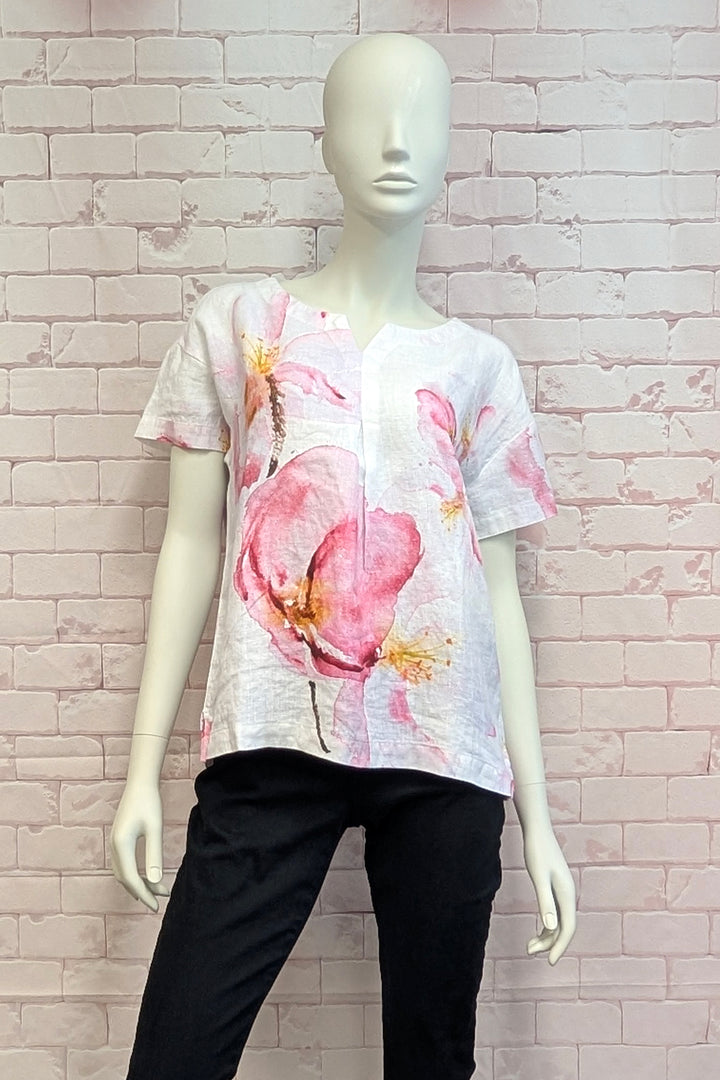 Mannequin wearing a floral blouse split neck with black pants against a light brick wall.