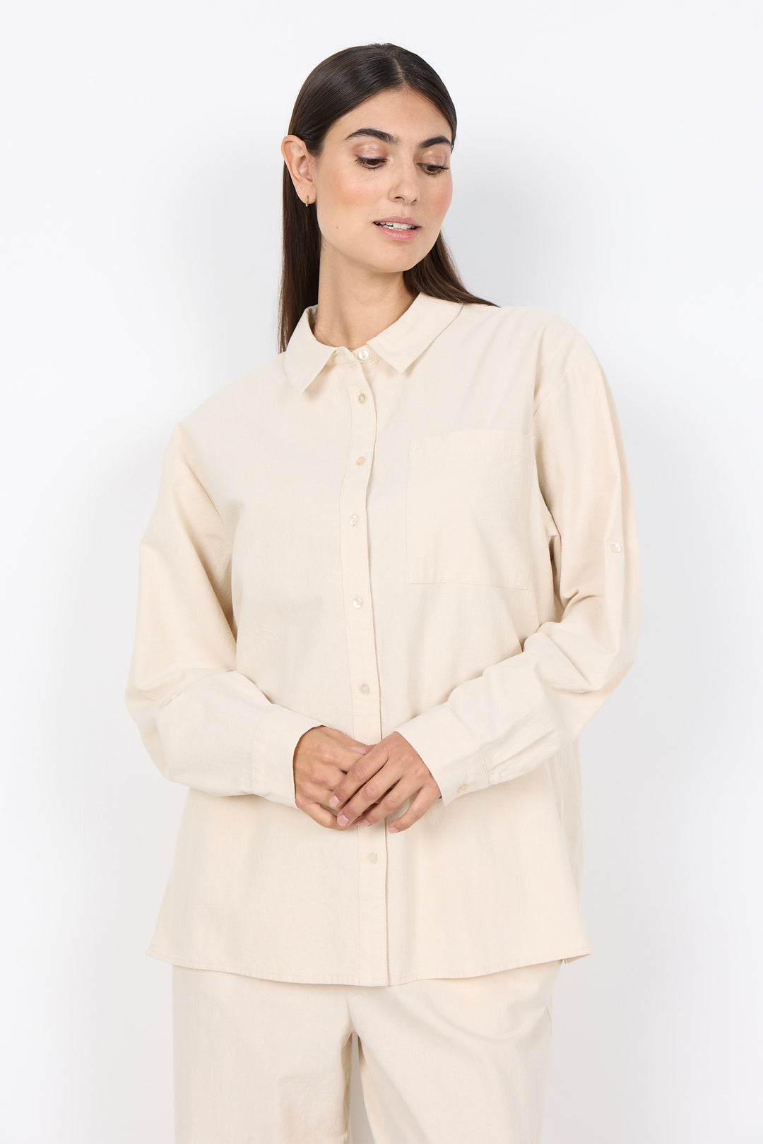 Woman wearing a beige cotton shirt and pants set against a white background