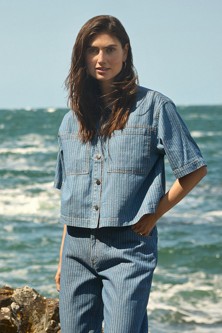 Woman wearing a blue denim cotton shirt standing by the ocean