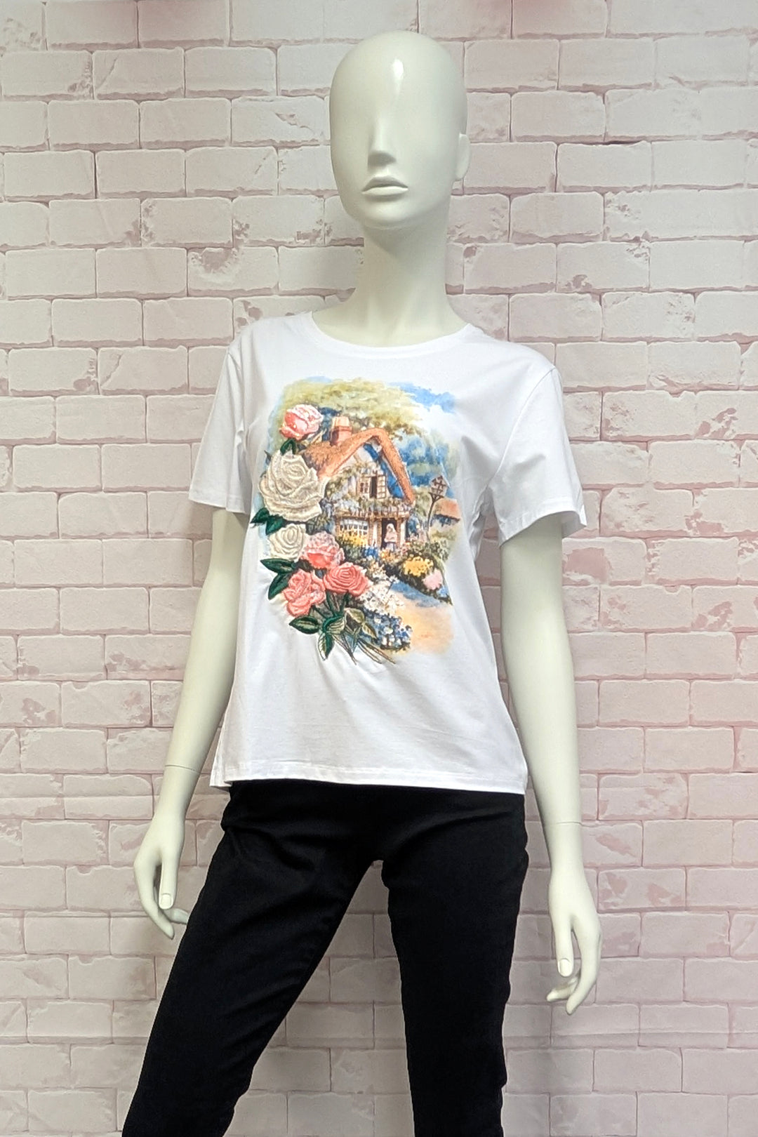 Mannequin wearing a white t-shirt with a colorful graphic design against a light brick wall.