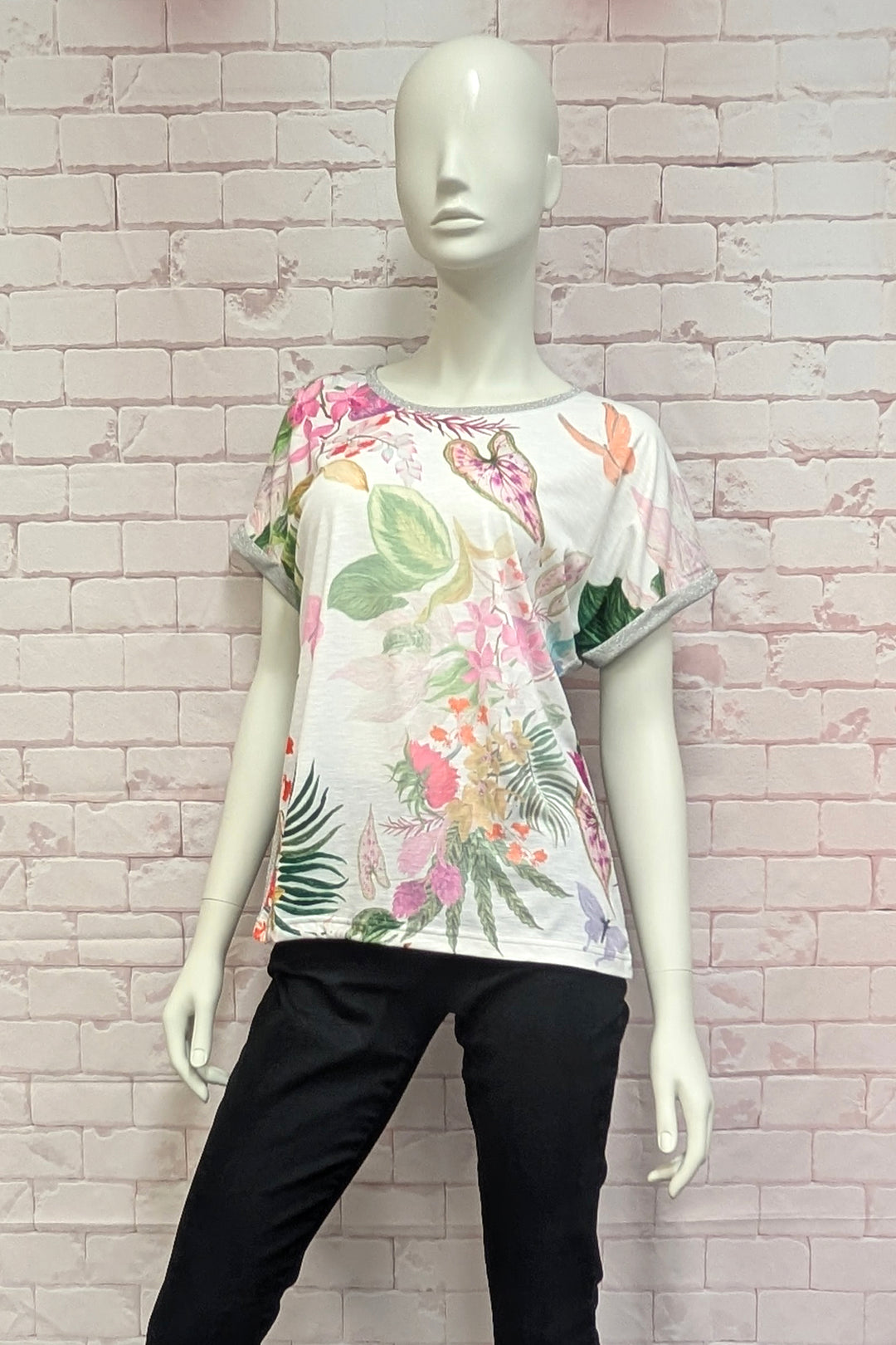 Mannequin wearing a floral top and black pants against a light brick wall.