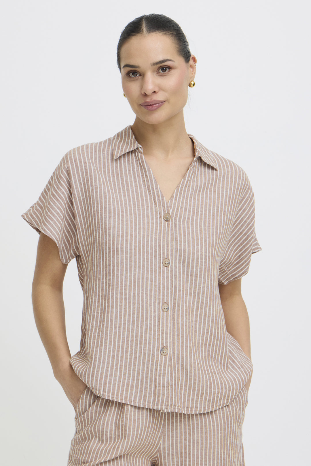 Woman wearing a beige striped short sleeve button shirt and pants on a white background