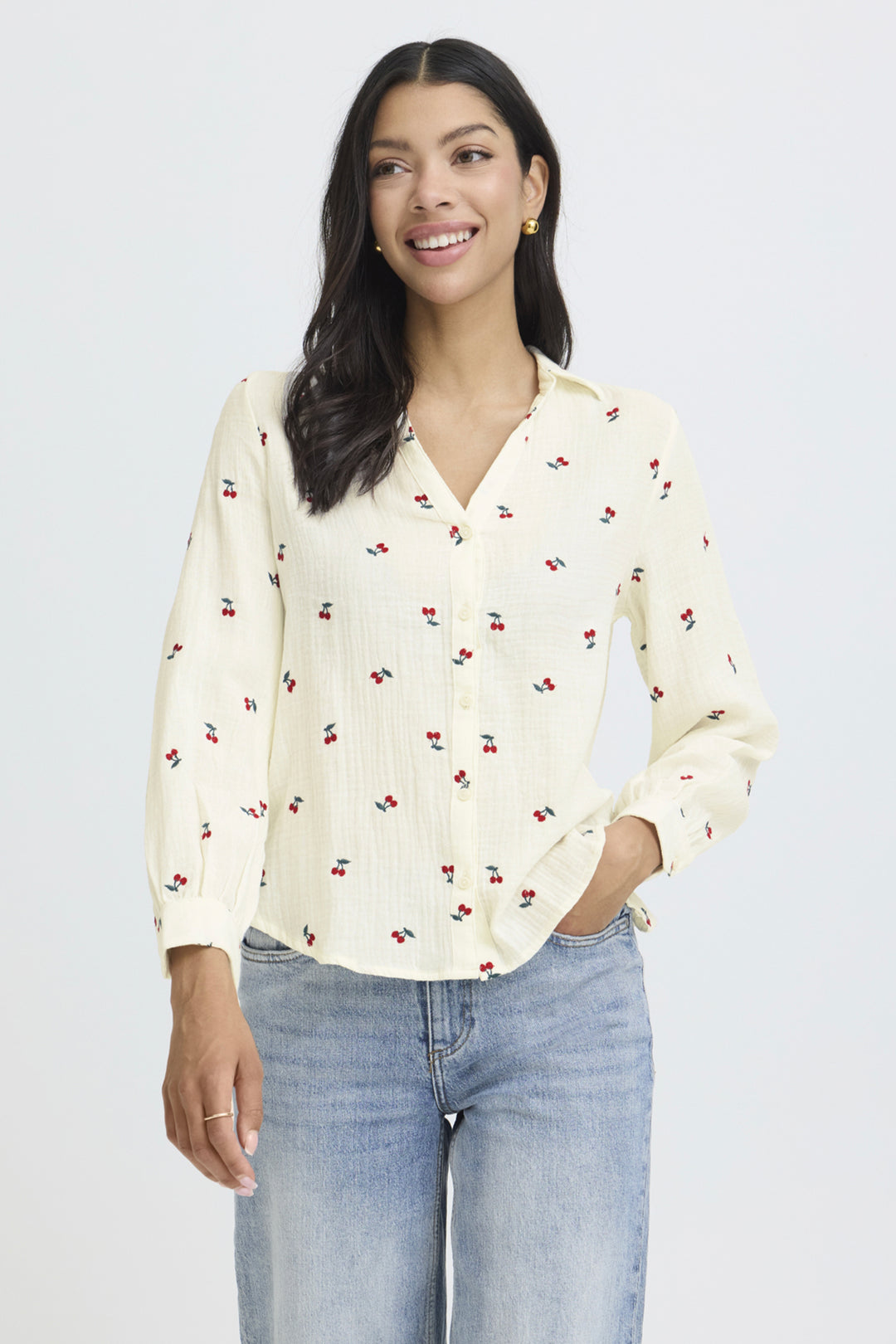 Woman wearing a cream blouse with cherry pattern and light blue jeans on a white background