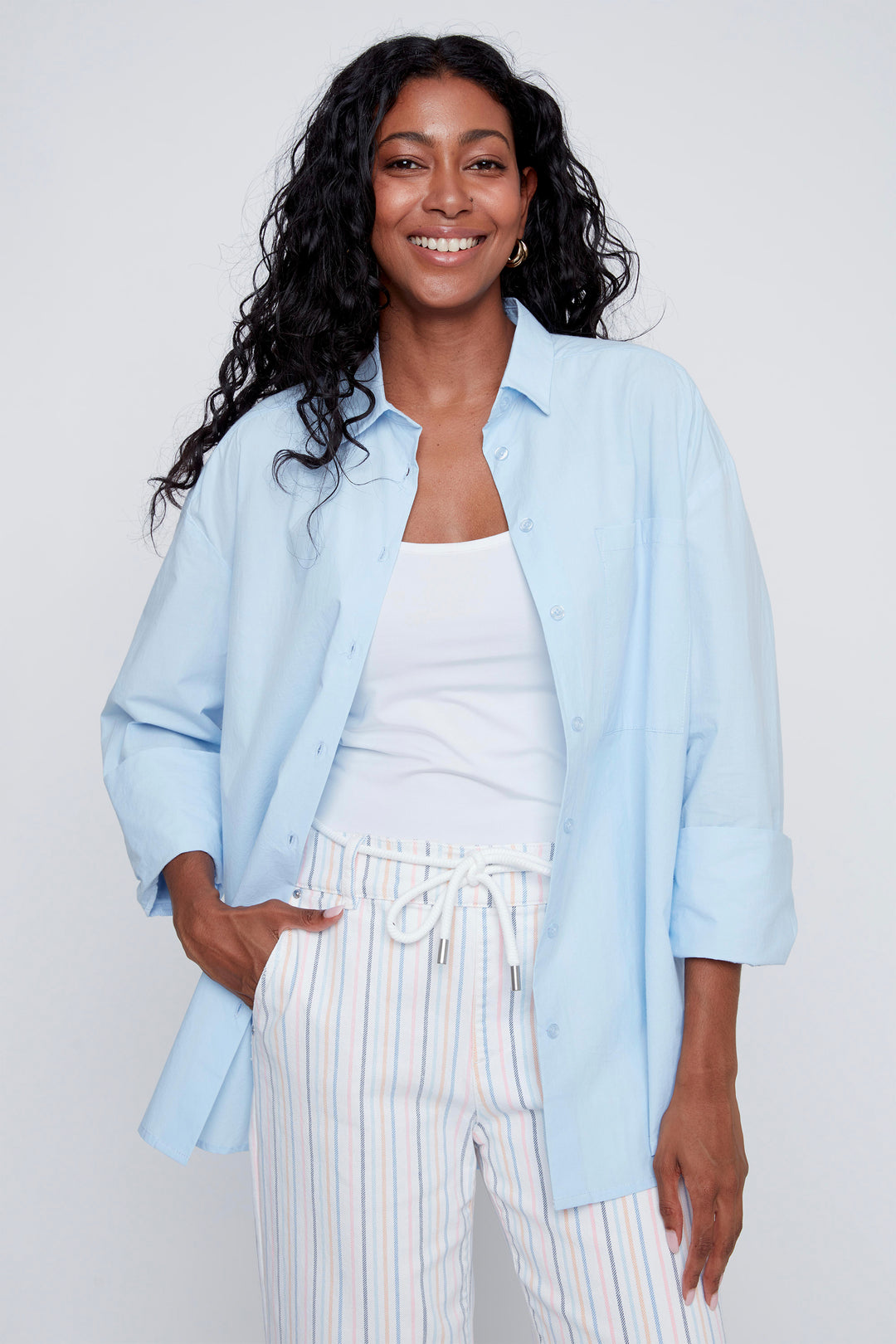 Woman wearing a light blue cotton dress shirt and striped pants against a white background