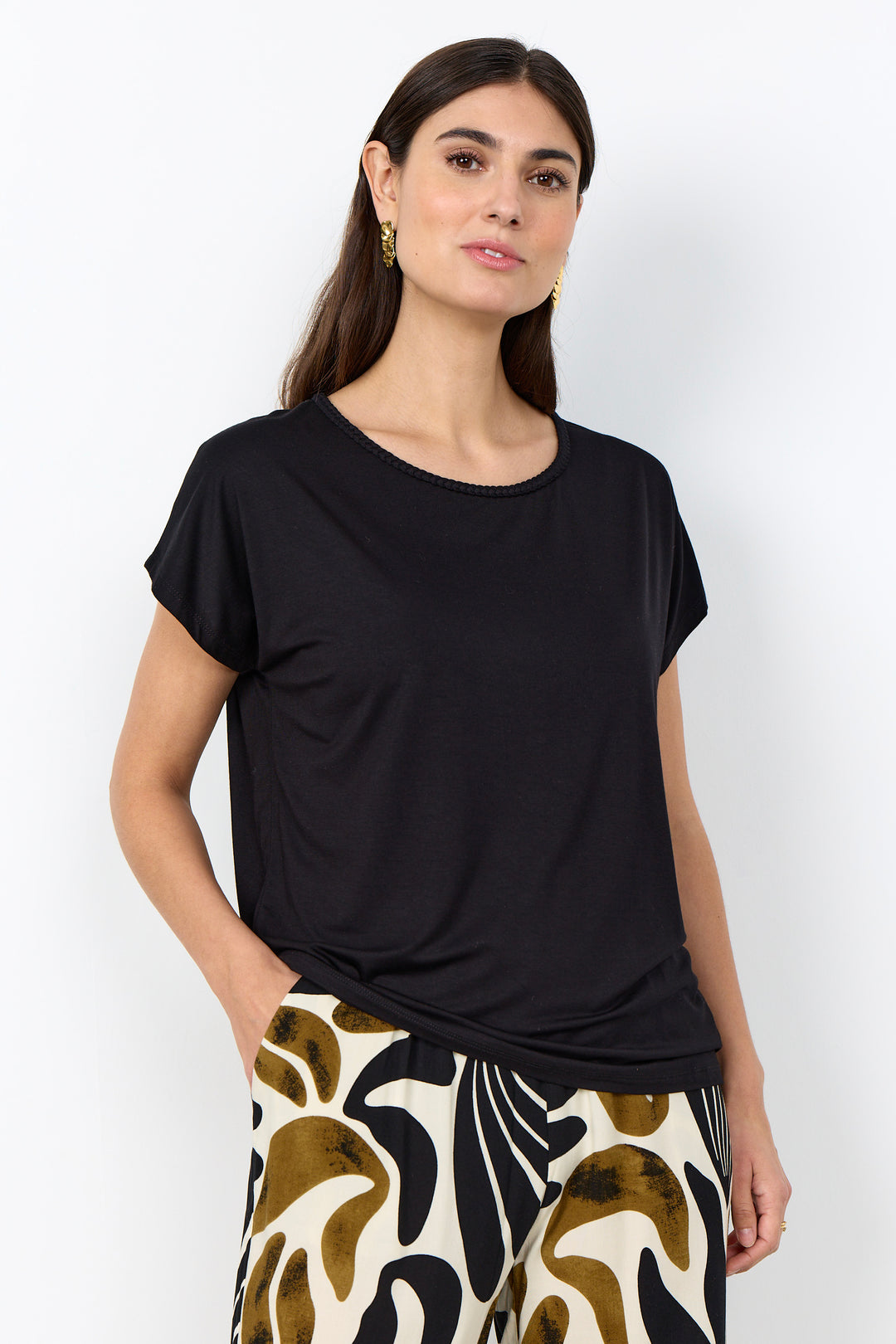 Woman wearing a black top with braided neckline and patterned pants on a white background