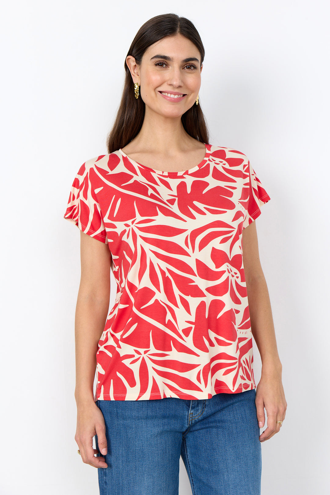 Woman wearing a red and white floral leaves top with blue jeans on a white background