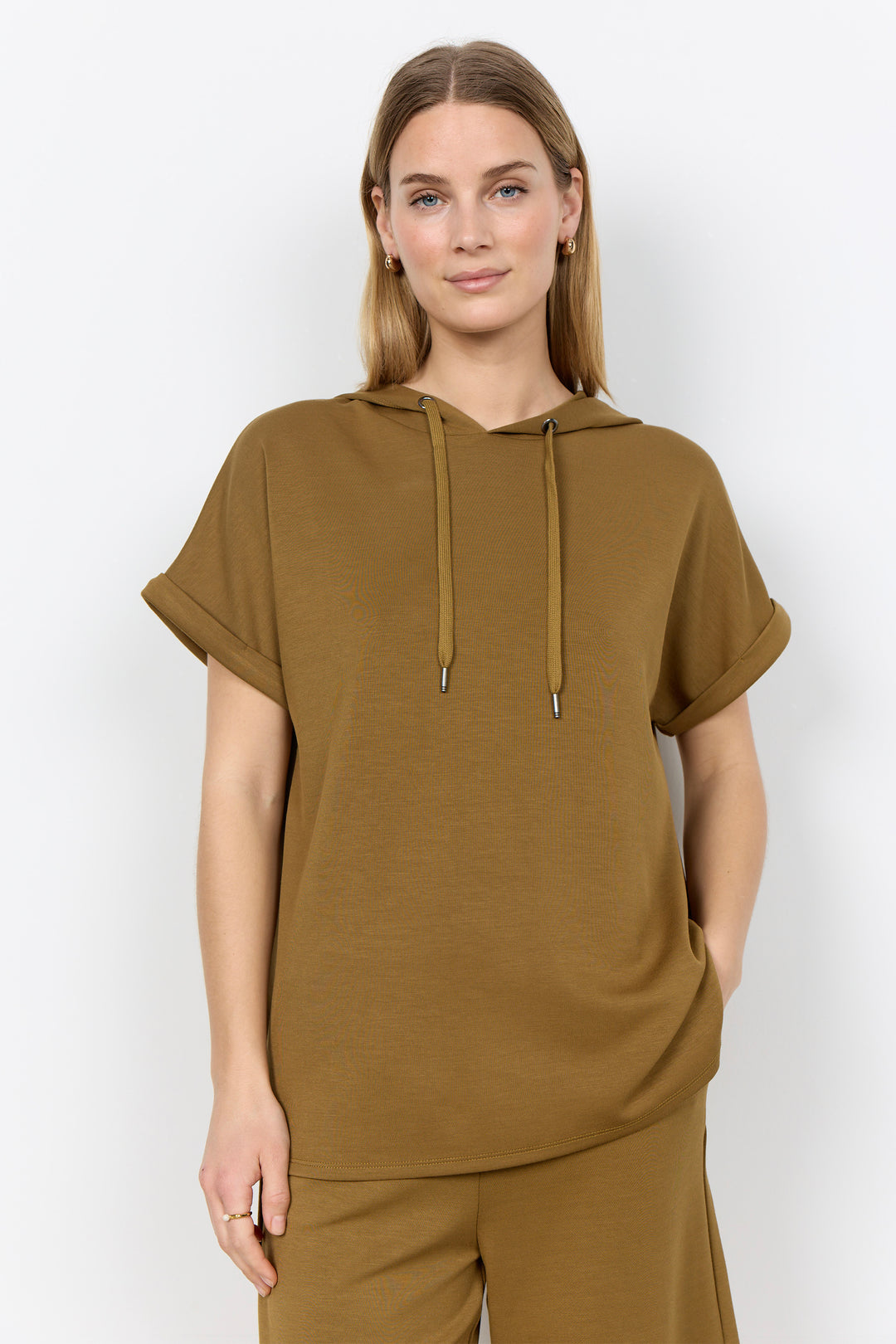 Woman wearing a brown hoodie with drawstring and short sleeves and pants against a white background