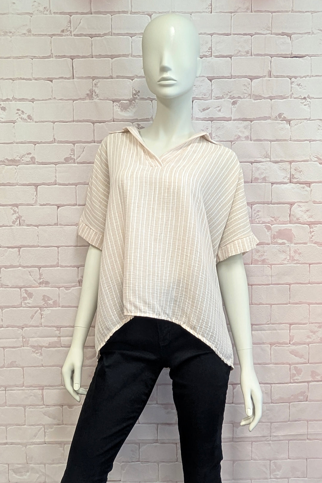 Mannequin wearing a striped oversized top and black pants against a white brick wall.