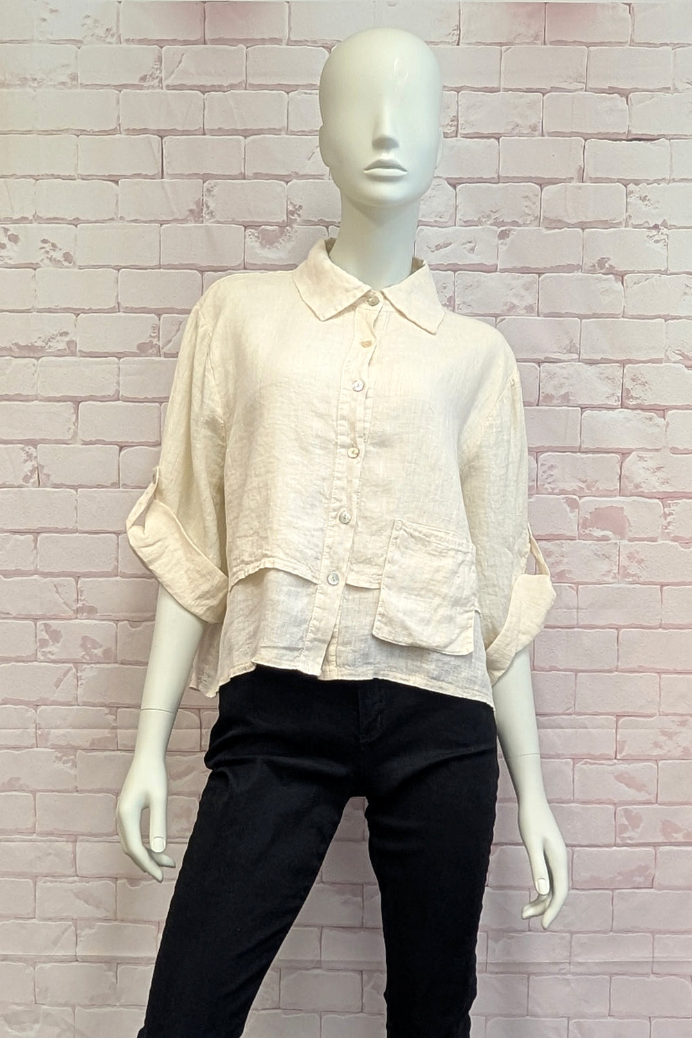 Mannequin wearing a cream blouse and black pants against a light brick wall.