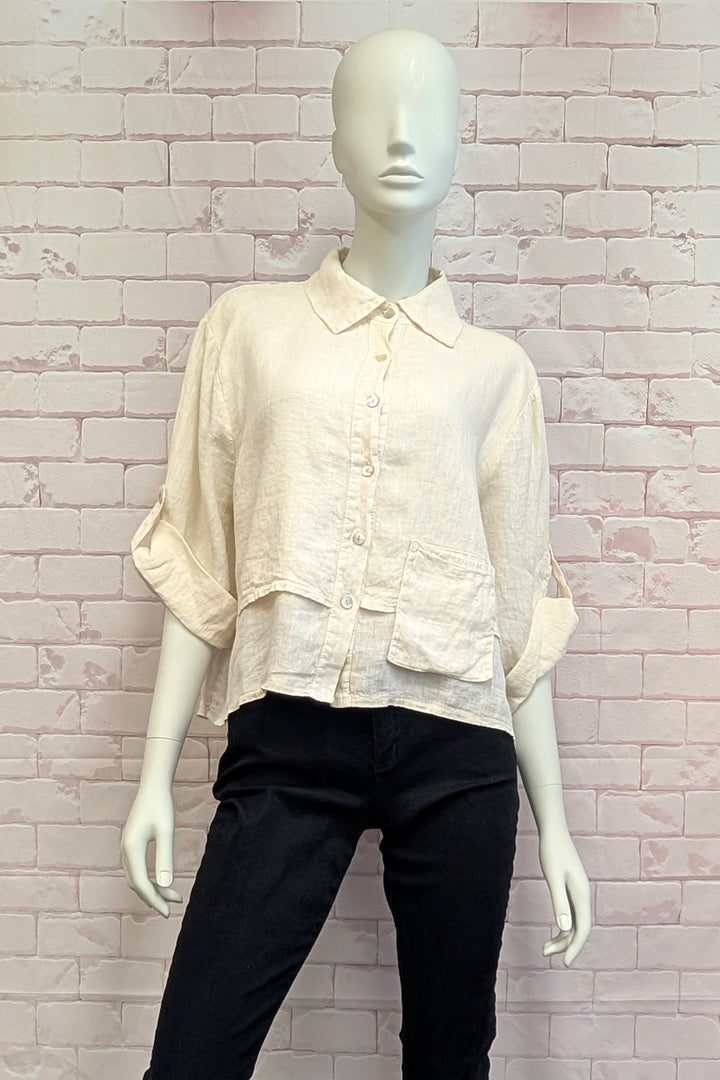 Mannequin wearing a cream blouse and black pants against a light brick wall.