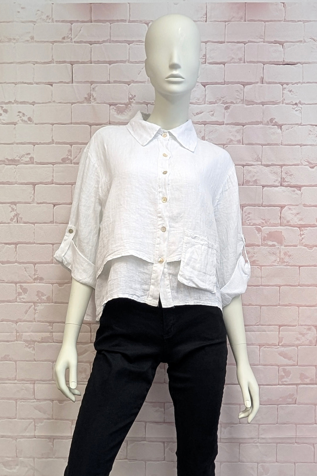 Mannequin wearing a white blouse and black pants against a light brick wall.