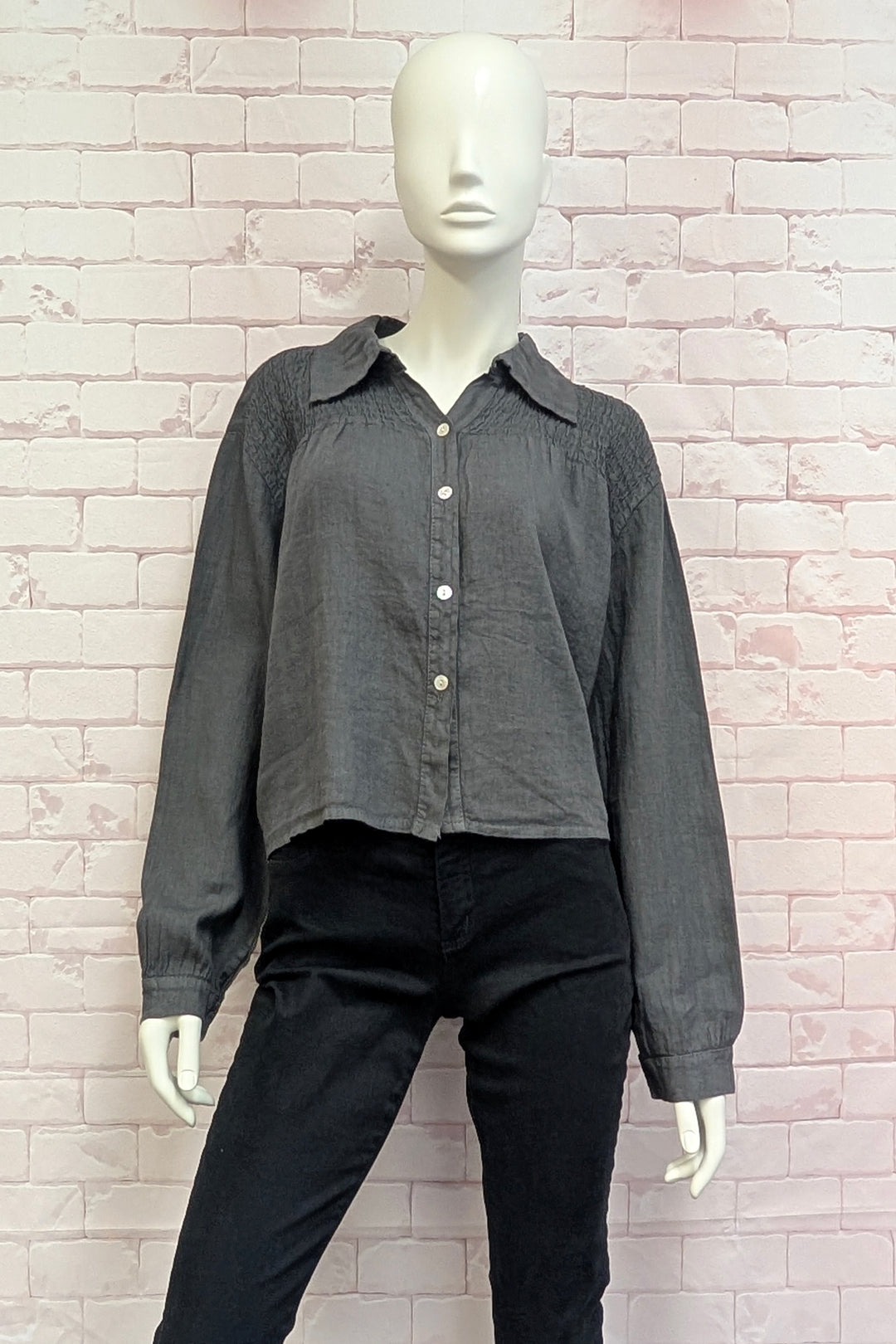 Mannequin wearing a gray button-up shirt and black pants against a brick wall.