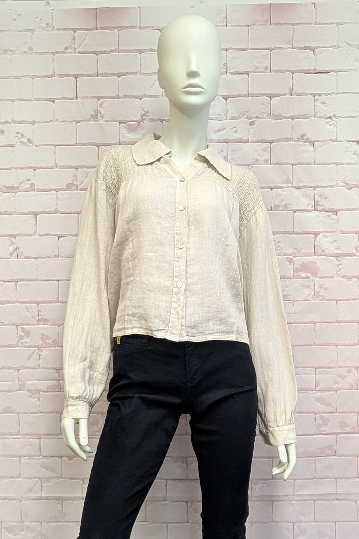 Mannequin wearing a light-colored blouse with a collar against a white brick wall.