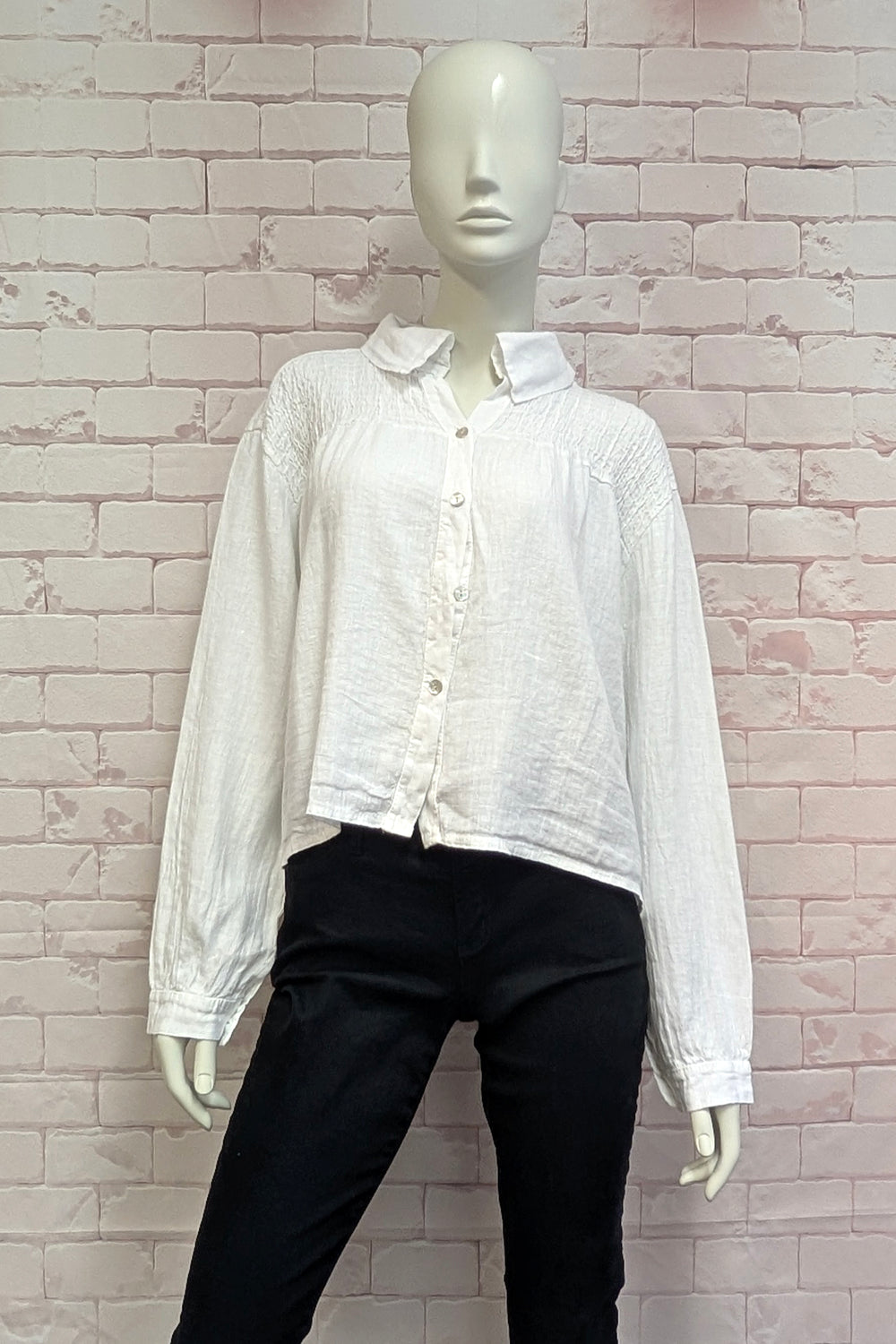 Mannequin wearing a white button-up shirt and black pants against a brick wall.