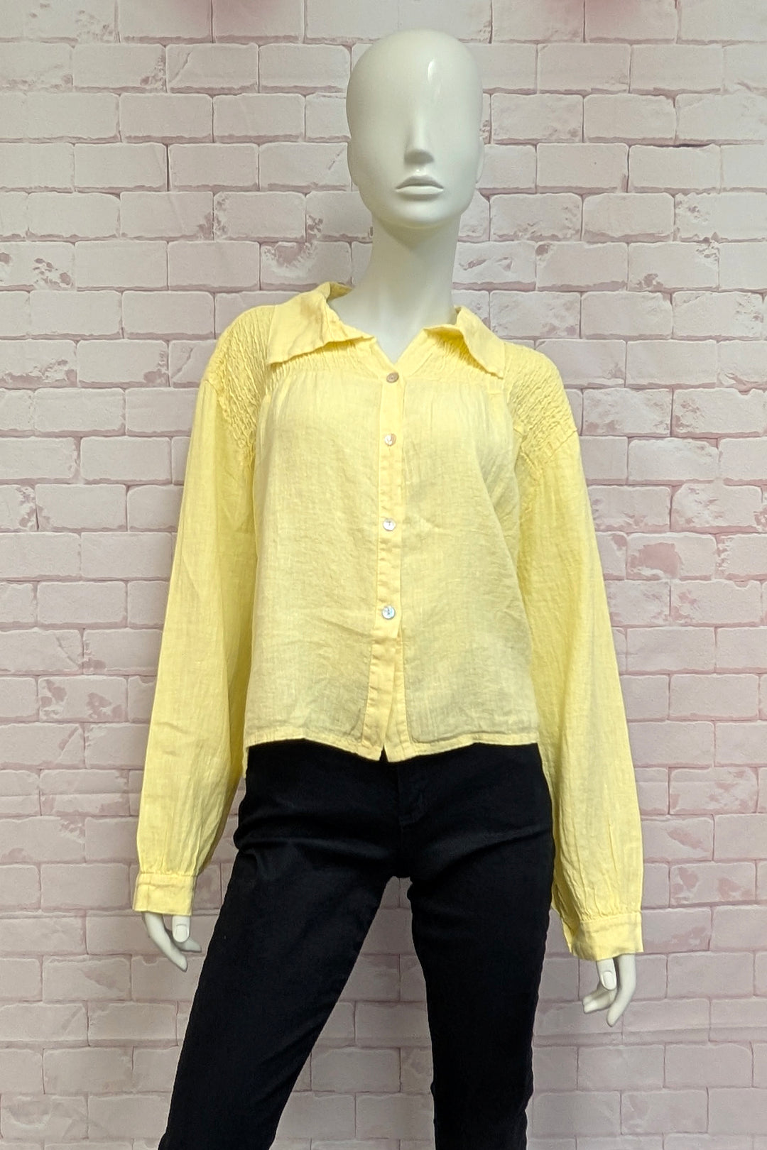 Mannequin wearing a yellow shirt and black pants against a light brick wall.
