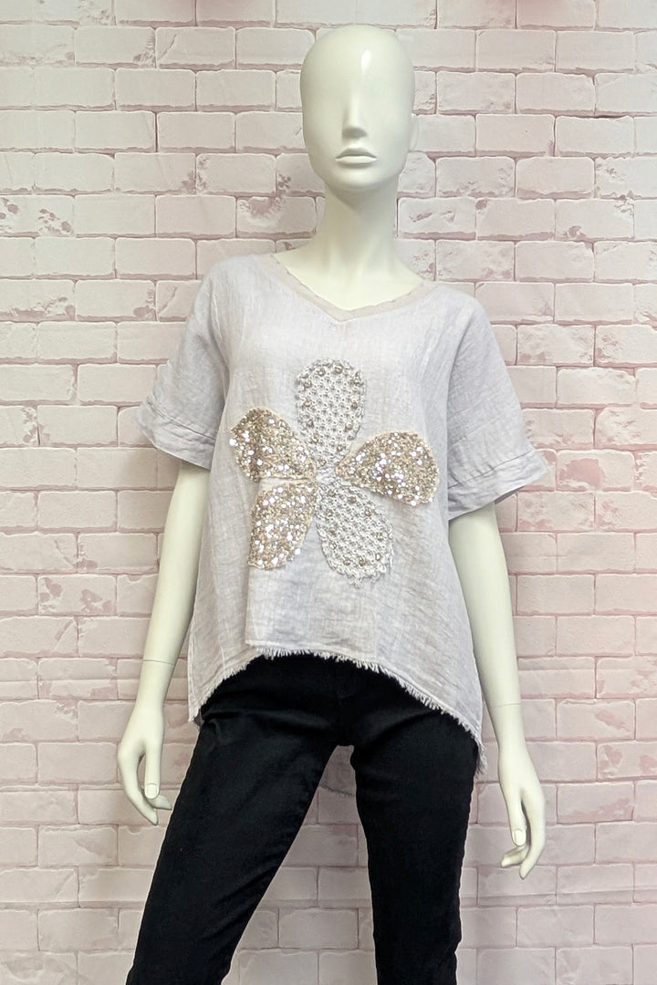 Mannequin wearing a light gray top with a decorative flower design against a brick wall.