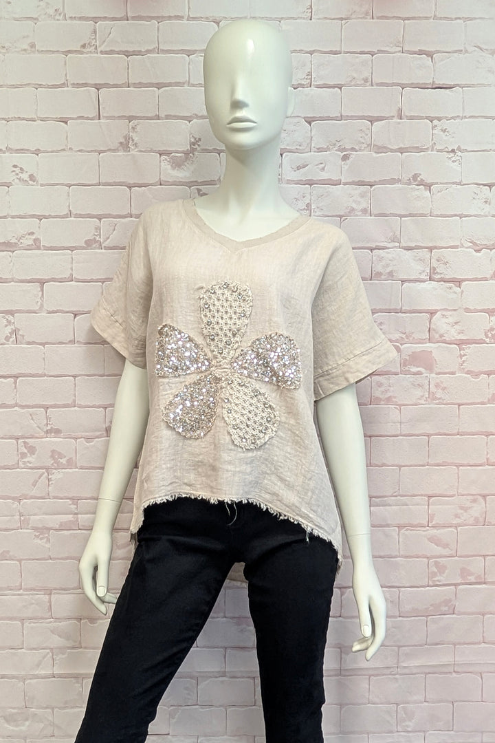 Mannequin wearing a beige t-shirt with a floral embellishment against a light brick wall.