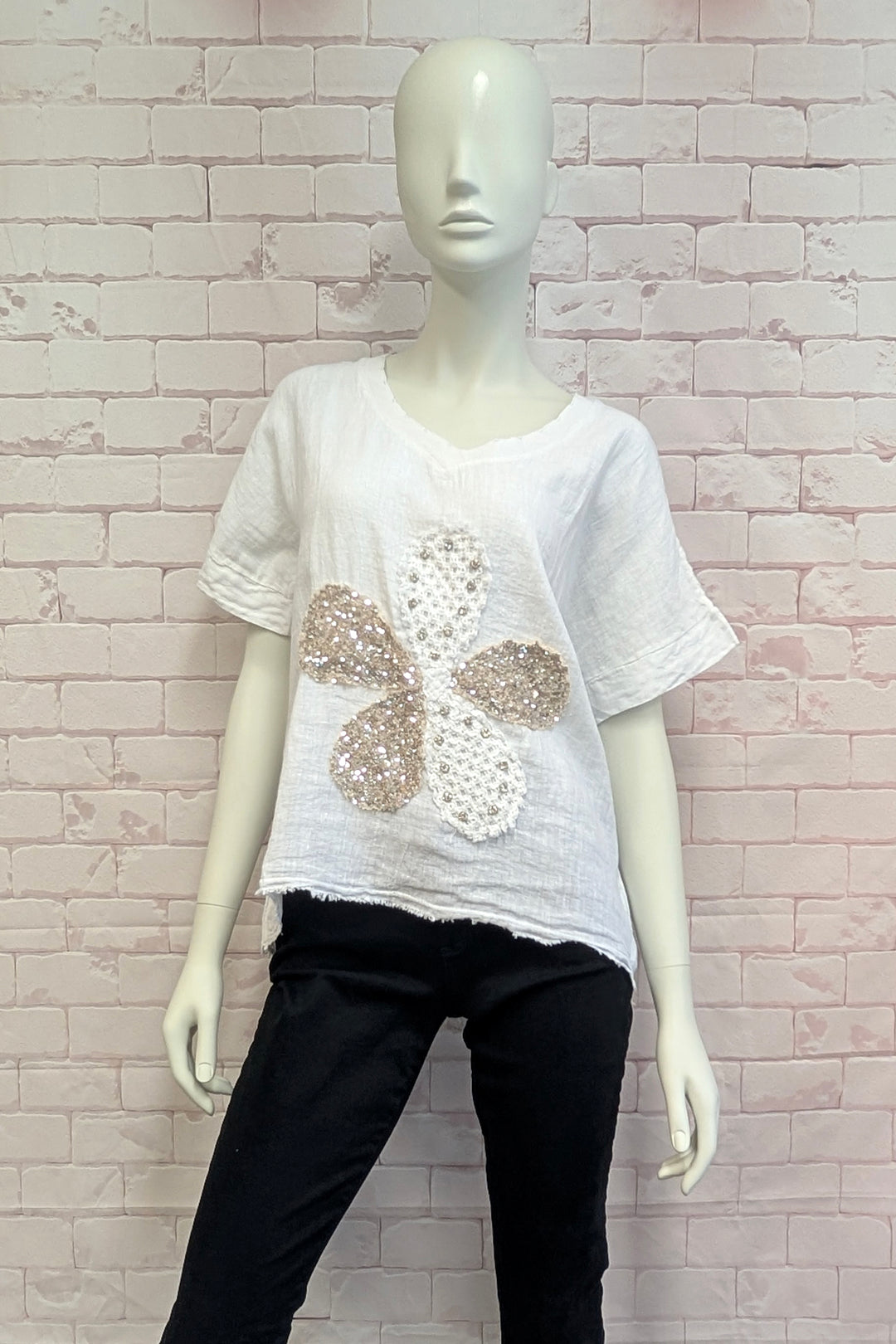 Mannequin wearing a white top with sequin flower design against a light brick wall.