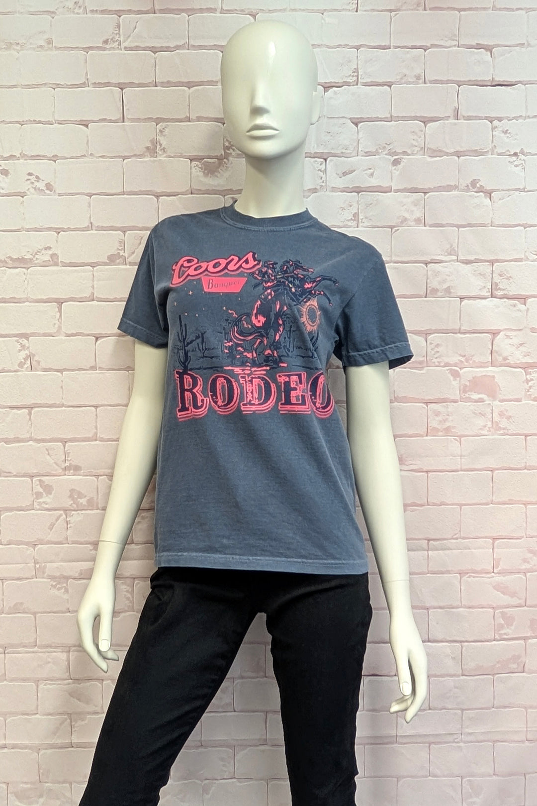 Mannequin wearing a gray t-shirt with red text and graphics against a light brick wall.