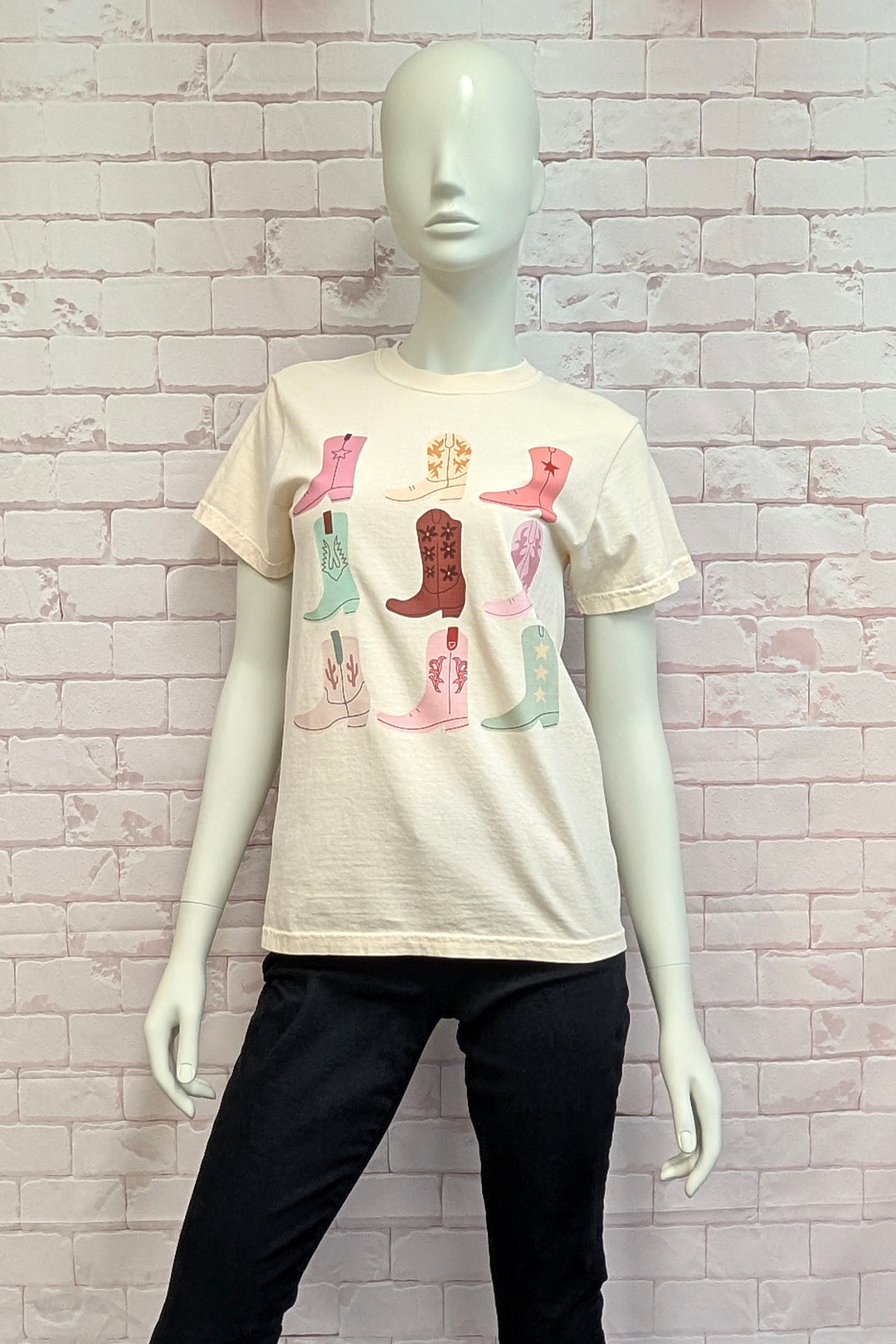 Mannequin wearing a cream t-shirt with colorful graphic design against a light brick wall.
